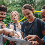 A diverse group of travelers planning their route on a map during a group tour in a tropical forest setting.